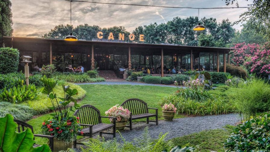 Exterior view of Canoe with a large green with all different types of plants and trees plus benches for sitting and a walk way in front of the entrance in Atlanta, Georgia, USA
