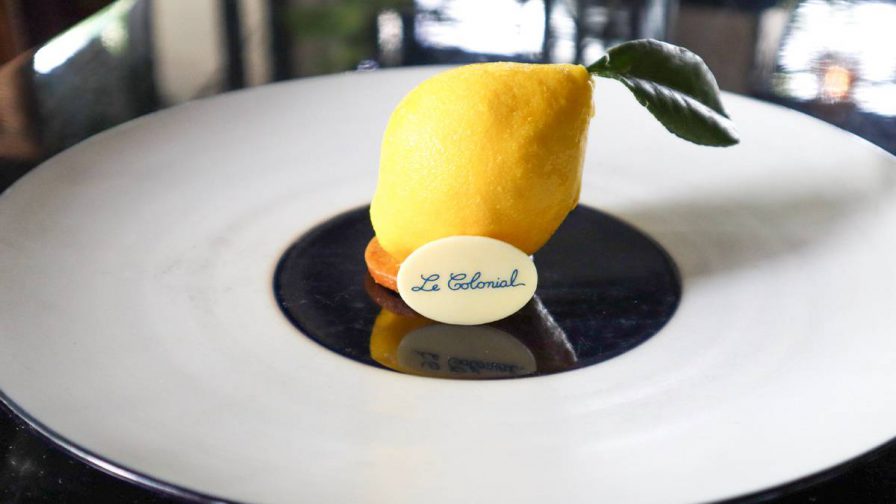A desert on a white plate that looks like a lemon with a piece of white chocolate that says Le Colonial at Le Colonial in Atlanta, Georgia, USA