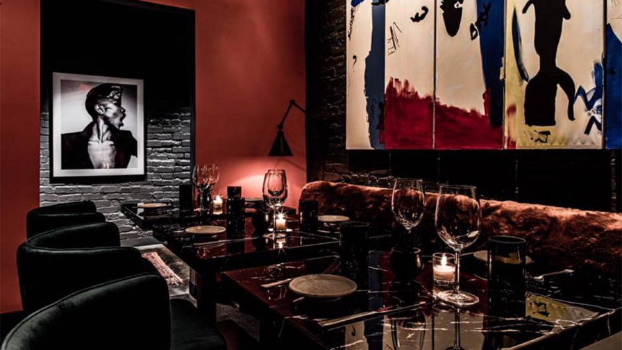 A dark dining area with black chained and abstract art on the walls with black marble tables with wine glasses on them at Rock Steady in Atlanta, Georgia, USA