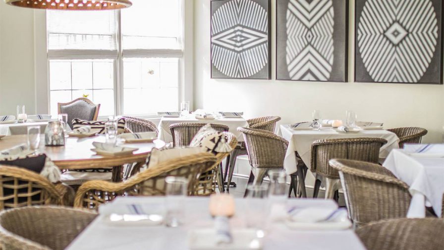 Dining room with white walls and tables with white cloths and wicker chairs at Yebo Beach Haus in Atlanta, Georgia, USA