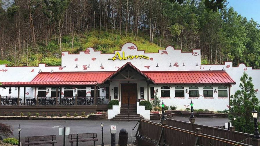 Wide shot of the front exterior of The Alamo Steakhouse, a white building with red accent and a red awning, in Gatlinburg, Tennessee, USA
