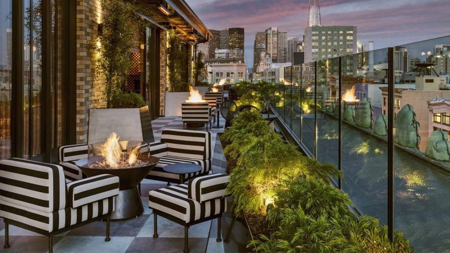 View of the outdoor lounge area with black and white stripped chairs with fire pits in the middle and plants lining the outer edge at Charmaine’s Rooftop Bar & Lounge in San Francisco, California, USA
