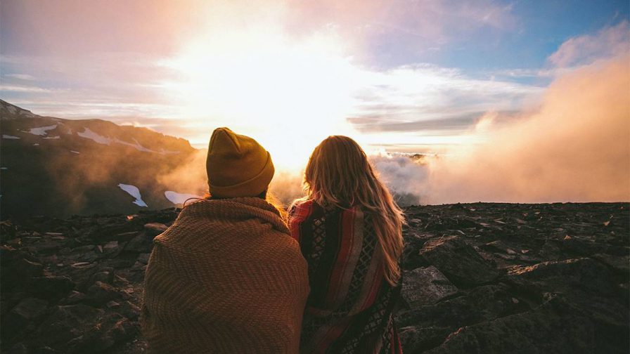 Couple wrapped in blankets facing away from the camera on Mt. Rainier with the sun shining inferno of them and lots of steam in Seattle, Washington, USA