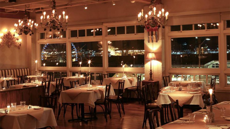 A dining room with table that have white cloths on them and is lit by low candle light at The Pink Door in Seattle, Washington, USA