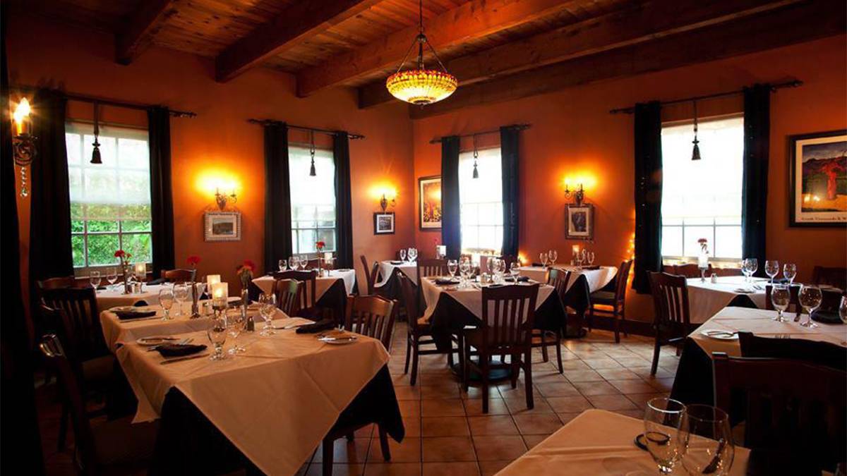 A low light dining room with wooden tables that have white tables clothes and candles on them at Collage Restaurant in St Augustine, Florida, USA