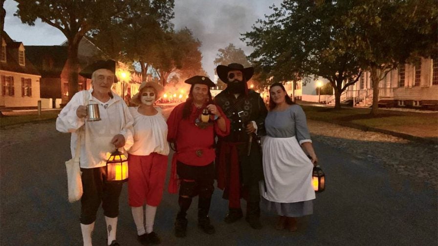Group of people dressed at pirates, ghosts, and witches on the The Ghosts, Witches, and Pirates of Williamsburg Tour with a fire behind them in Williamsburg, Virginia, USA
