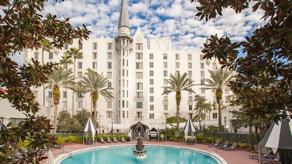 exterior of Castle Hotel Autograph Collection with fountain and trees during cloudy day in Orlando, Florida, USA