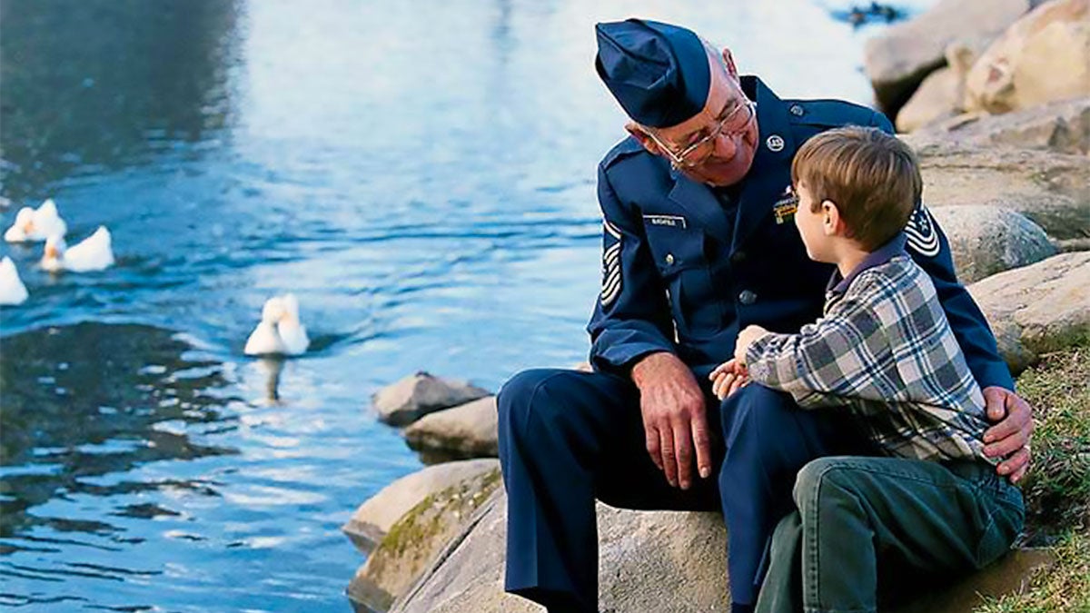 child and grandparent in uniform seated on rocks by water with ducks in Pigeon Forge, Tennessee, USA