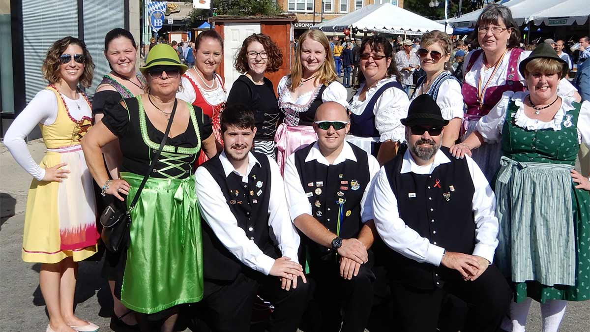 group of people posing for photo in festive attire with stalls in background at Chicago German-American Oktoberfest in Chicago, Illinois, USA
