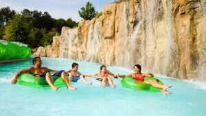 family on swim rings holding hands on blue pool with waterfalls on side at Downbound Float Trip in Dollywood Splash Country, Pigeon Forge, Tennessee, USA