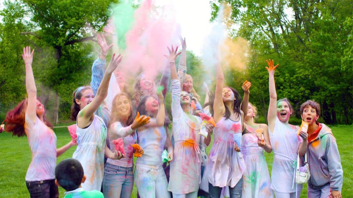 group of children outdoors in light clothing tossing colored powder for Holi Festival Of Colors in Illinois, USA