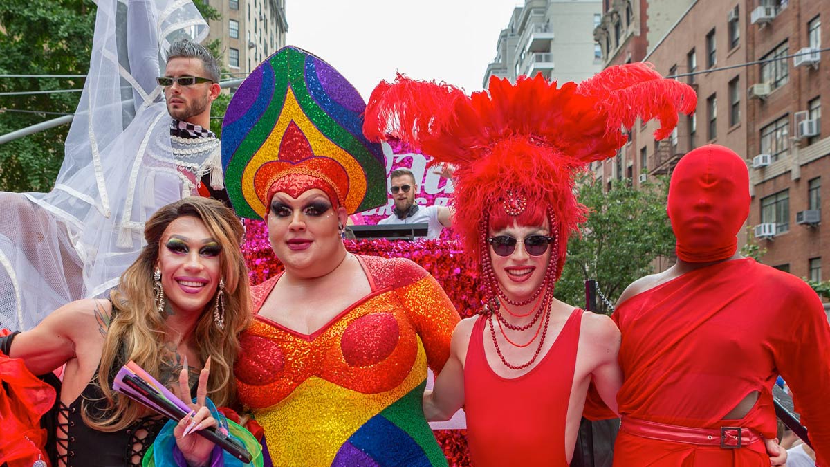 Four LGBT individuals wearing red outfits are shown in a group photo with two other males at the back.