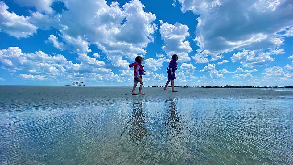 children playing in shallow coastal water under a blue sky with clouds at new smyrna beach