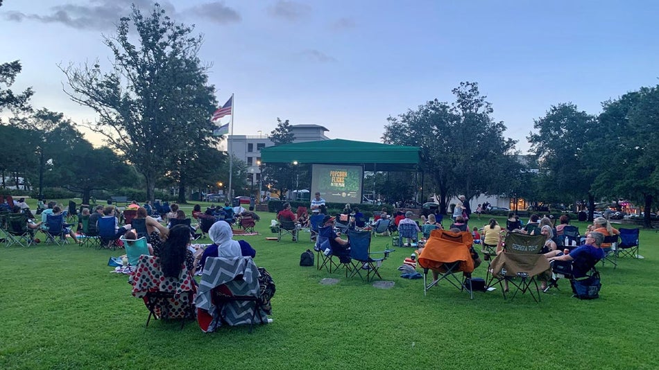 people seated on foldable chairs gathered at park watching screen with trees in background for Popcorn Flicks in the Park in Winter Park, Florida, USA