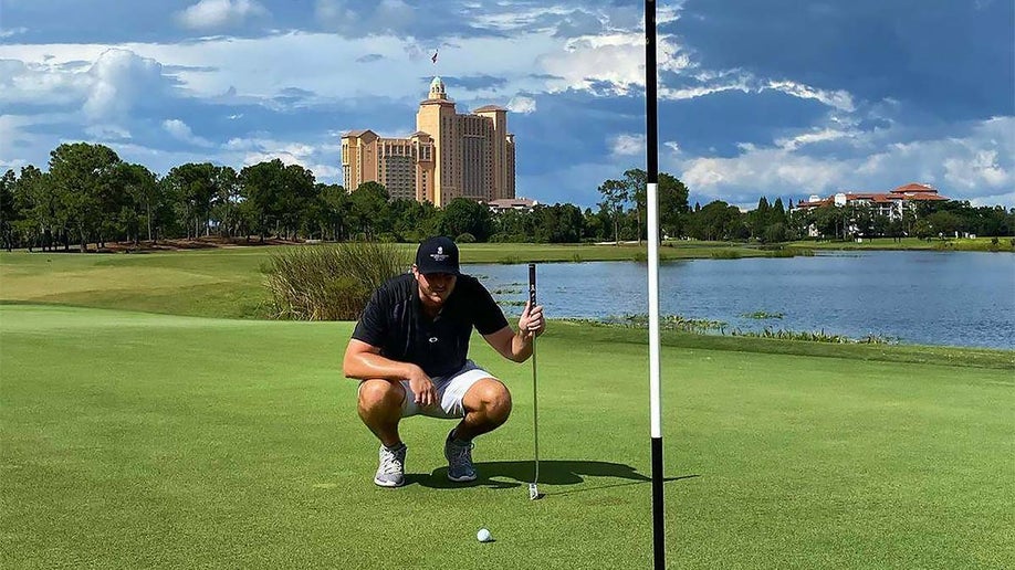 man crouched holding golf club looking at golf ball with water, trees in background and building in distance at The Ritz-Carlton Golf Club Grande Lakes in Orlando, Florida, USA