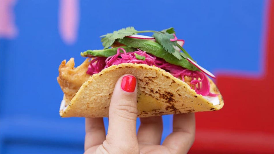 close up of person holding taco against blue and red wall at Black Rooster Taqueria in Orlando, Florida, USA