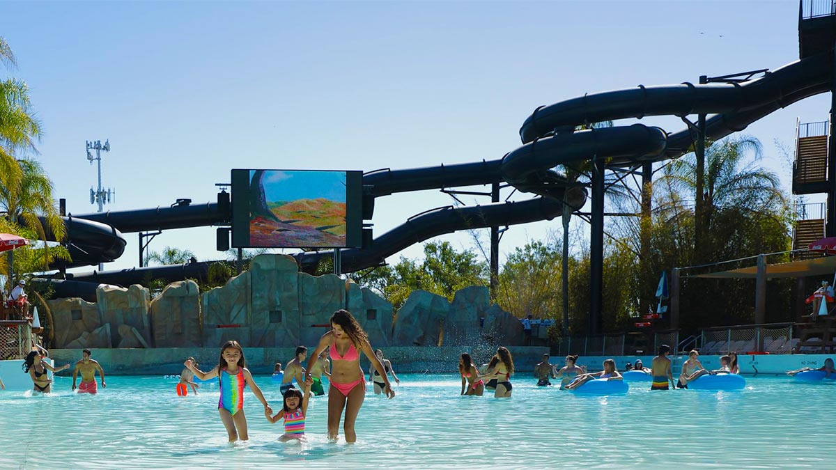 Families in a shallow pool at Six Flags Hurricane Harbor with a water slide in the background