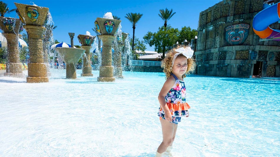 child standing in shallow pool with fountain in the background at Bombs Away Bay at Big Kahuna's in Destin, Florida, USA