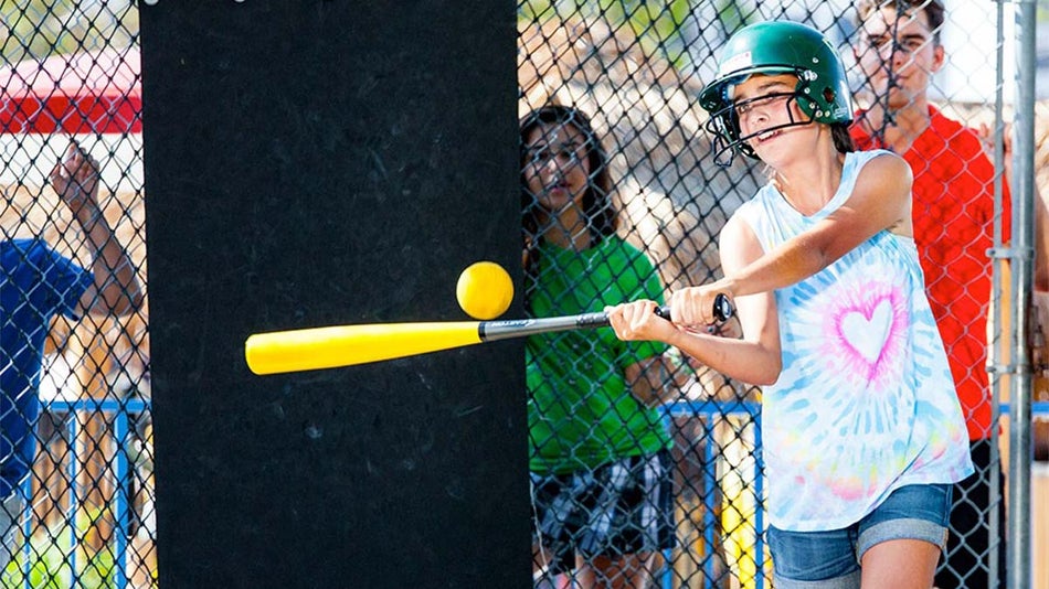 girl in helmet hiting ball with baseball bat with friends watching outside at Batting Cages in Boomers Livermore, San Francisco, California, USA