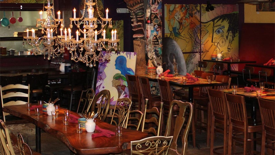 wooden dining tables and chairs at interior of Cafe Tu Tu Tango decorated with chandeliers and colorful artwork in Orlando, Florida, USA