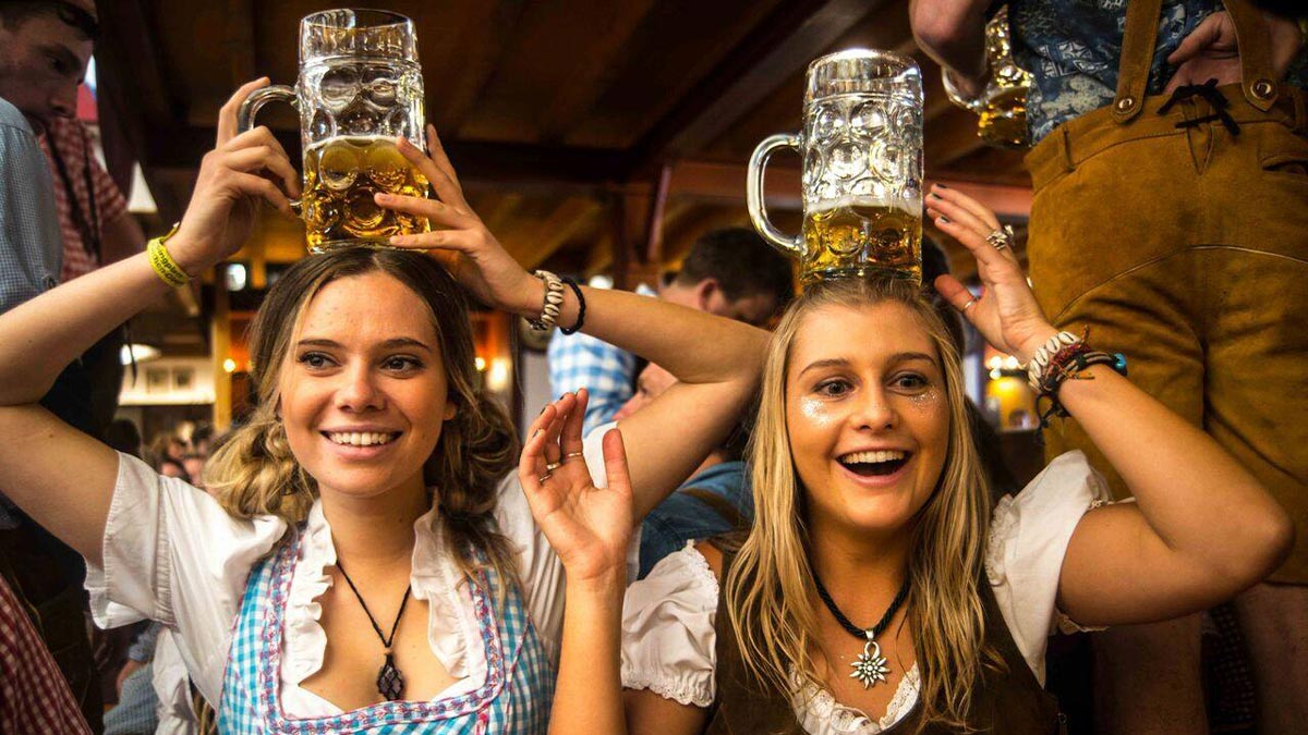 close up of two women in festive attire holding beer glasses over their heads at El Cajon Oktoberfest in San Diego, California, USA