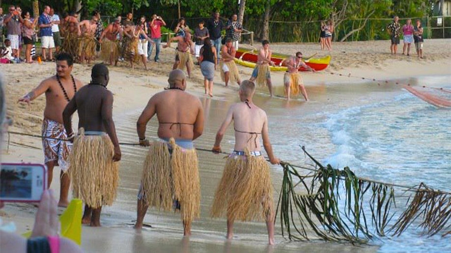 group of people performing Hukilau Ceremony on shore with crowd watching at Paradise Cove Luau in Oahu, Hawaii, USA
