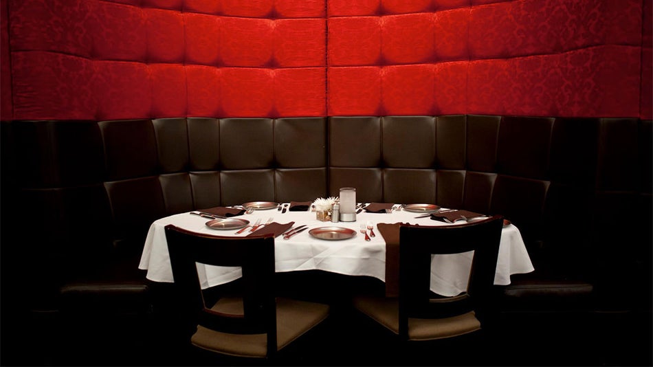 booth with red and black cushioned walls and set table covered in white cloth with two chairs at Kres Steakhouse in Orlando, Florida, USA