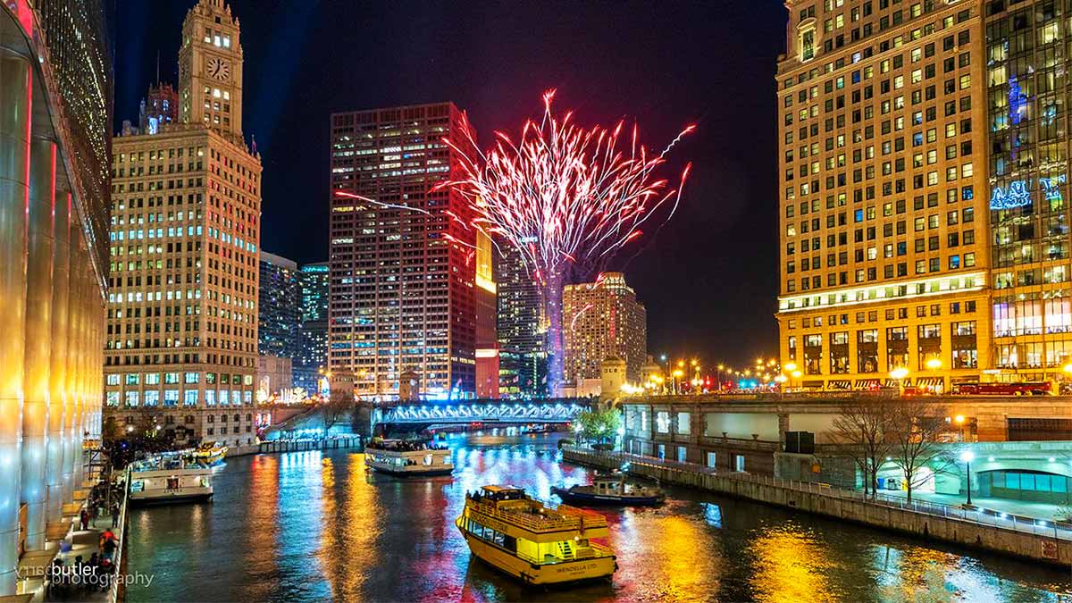 boats on water between building with red fireworks in sky at night at Magnificent Mile Lights Festival in Chicago, Illinois, USA