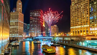 boats on water between building with red fireworks in sky at night at Magnificent Mile Lights Festival in Chicago, Illinois, USA