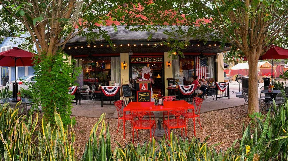 exterior of Maxines on Shine surrounded by trees and plants with two people seated at outdoor area in Orlando, Florida, USA