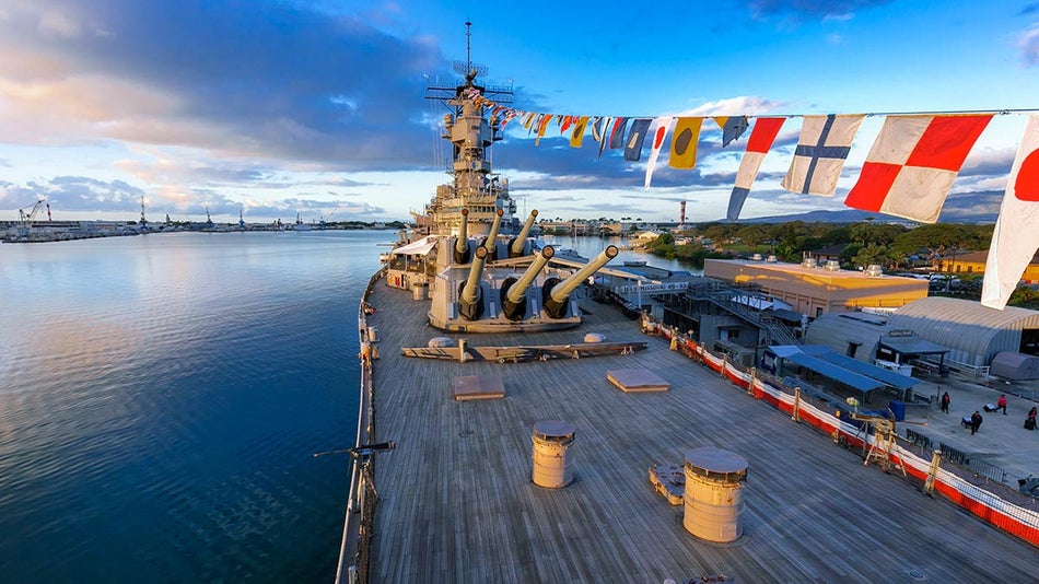 top deck of the USS Battleship missouri flags strung from the top of the guns with water surrounding under a twilight sky in Oahu, Hawaii 