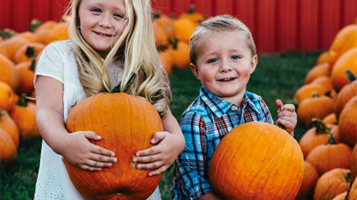 two smiling kids holding huge pumpkins