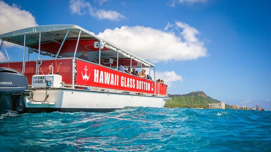 wide shot of a red and white hawaii glass bottom boat in the ocean with Diamond head in the background