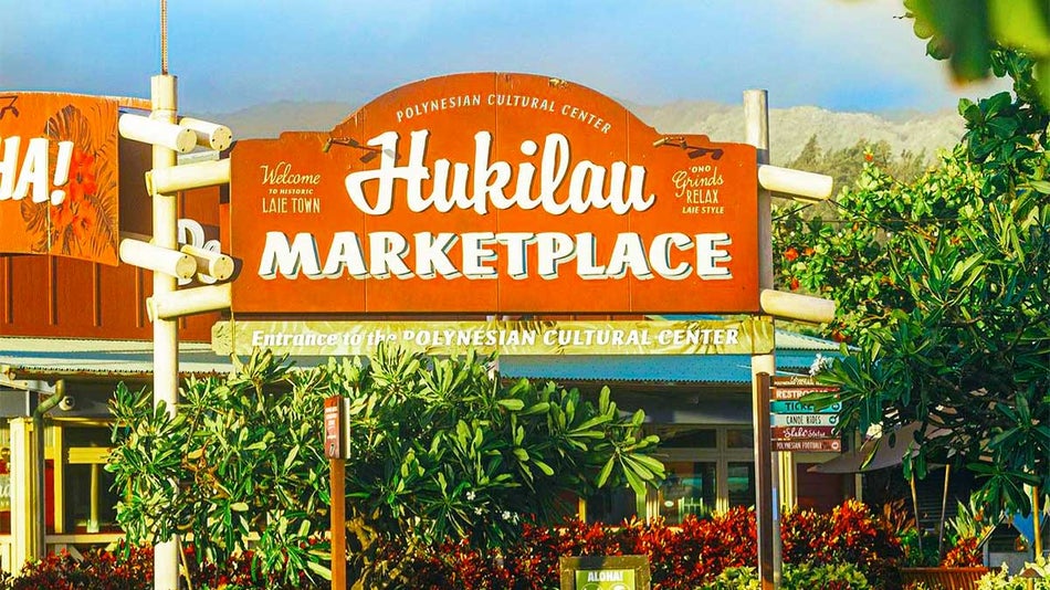 large entrance sign of Hukilau Marketplace surrounded by plants at Polynesian Cultural Center in Oahu, Hawaii, USA