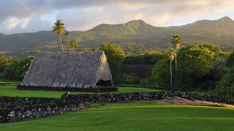 hut in field with trees in background and mountains in distance on sunny day at Kahanu Garden and Piilanihale Heiau at Road to Hana in Maui, Hawaii, USA