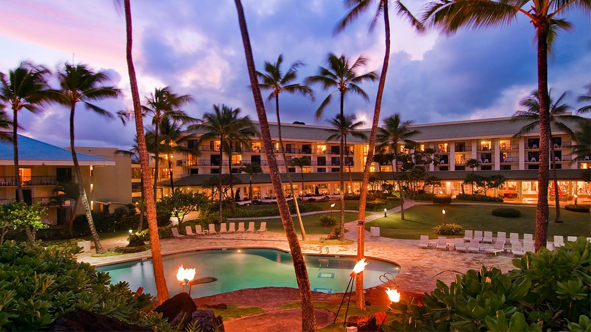 A photograph of a resort and spa taken near sunset, with the pool, large yard, and building visible. 