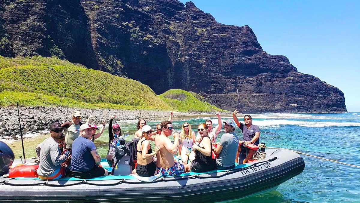 people on boat on water near shore with mountain in background at Kauai Sea Tours Na Pali Coast Beach Landing Day Raft Adventure in Kauai, Hawaii, USA