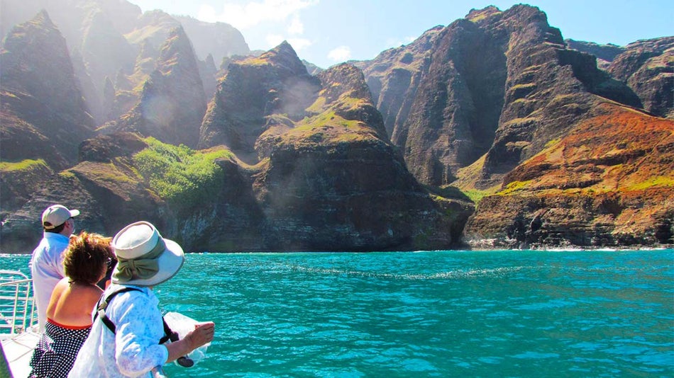 Tourists on the yacht are enjoying the beautiful scenery of the Na Pali Coast.