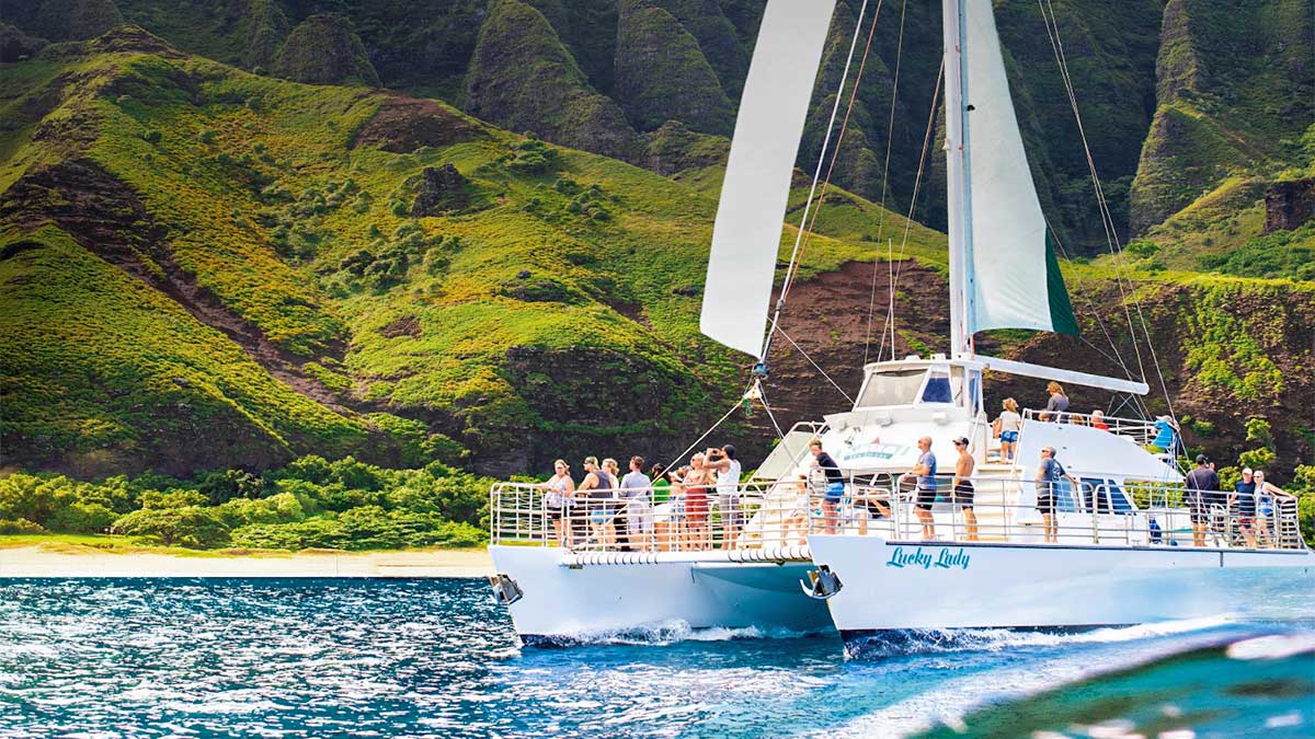 a semi front view of a sailing white yacht where tourist are enjoying the view of Kauai sea