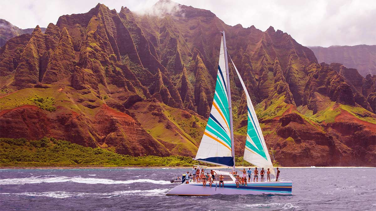 A view from a great distance of a sailing vessel at Napali Coast with several persons enjoying the ride.