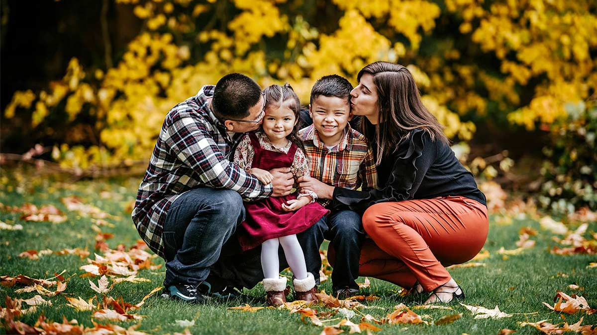 family of four posing for photo with trees in background and leaves on ground during fall at Lincoln Park Seattle in Seattle, Washington, USA