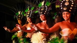 Five beautiful, smiling ladies perform a Hawaiian dance in Hawaiian attire.
