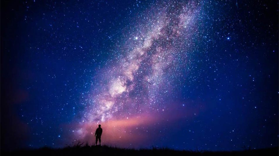 Silhouette of a person standing under a dark sky with the milky way illuminated 