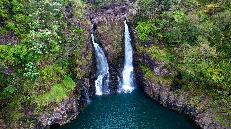 two twin waterfalls pouring into a dark blue lagoon surrounded by greenery covered bluff walls