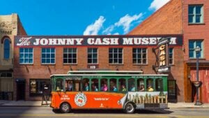 tourists aboard bus for Nashville Hop On Hop Off Trolley Tour with Johnny Cash Museum in background on sunny day in Nashville, Tennessee, USA