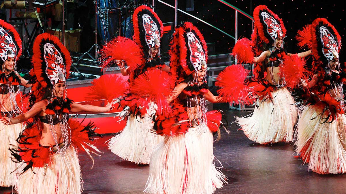 A group of females are dancing on the stage and have a red costume on it.