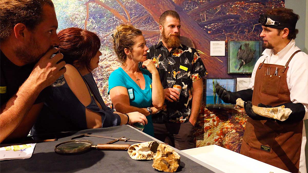 Four tourists listen to the explanation of the staff of the museum about the bones of a specie.