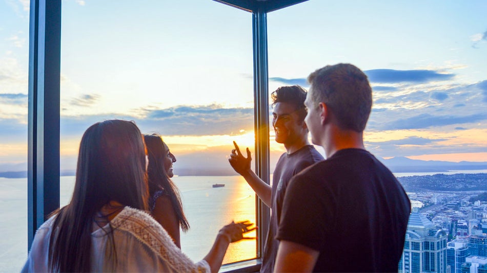 friends looking at view with water and sun shining through clouds and buildings on the side through Skyview Observatory in Seattle, Washington, USA