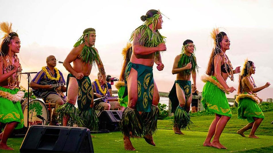 a group of performers in green Hawaiian attire, seven of them are dancing and others are singing.