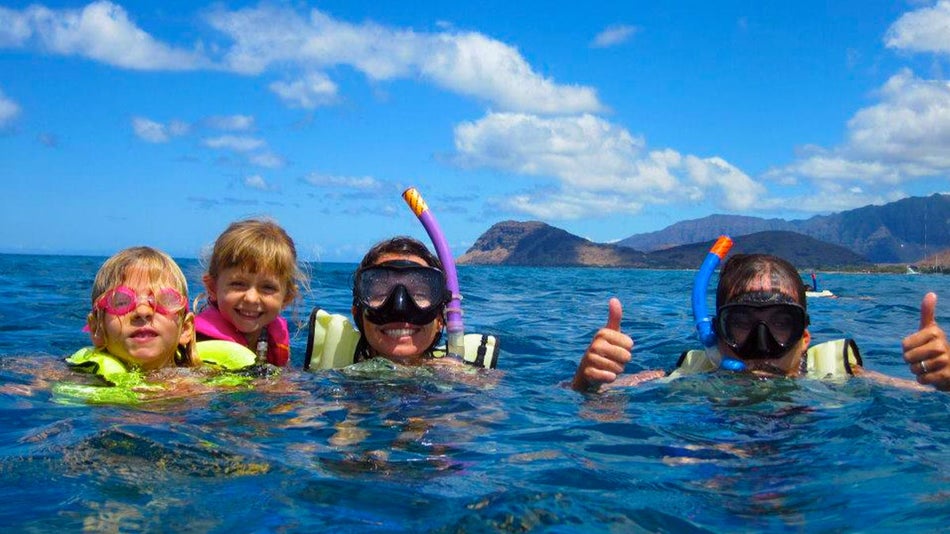 family in water with snorkeling gear during day with mountain in background at West Oahu Ocean Playground Snorkel with Hawaii Nautical in Oahu, Hawaii, USA